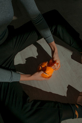 High angle view of cropped hands peeling orange in darkroom
