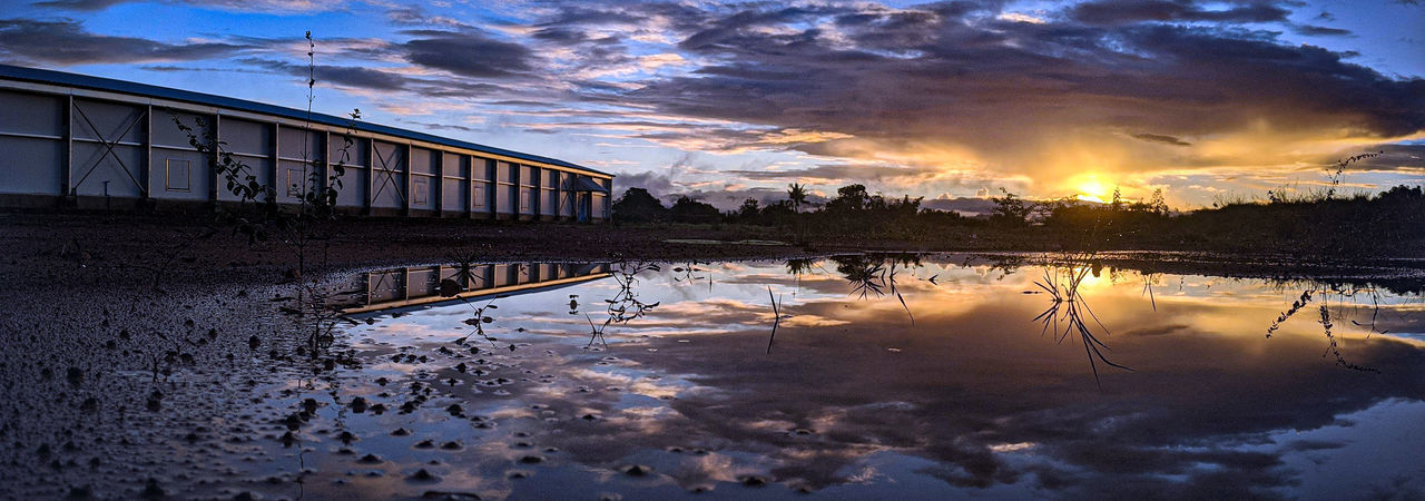 Scenic view of lake by buildings against sky during sunset