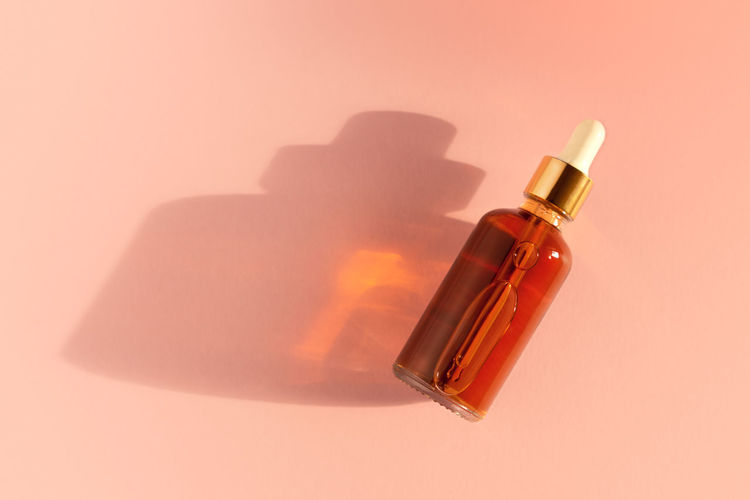Transparent amber green glass dropper bottles with liquid inside on beige background in the sunlight
