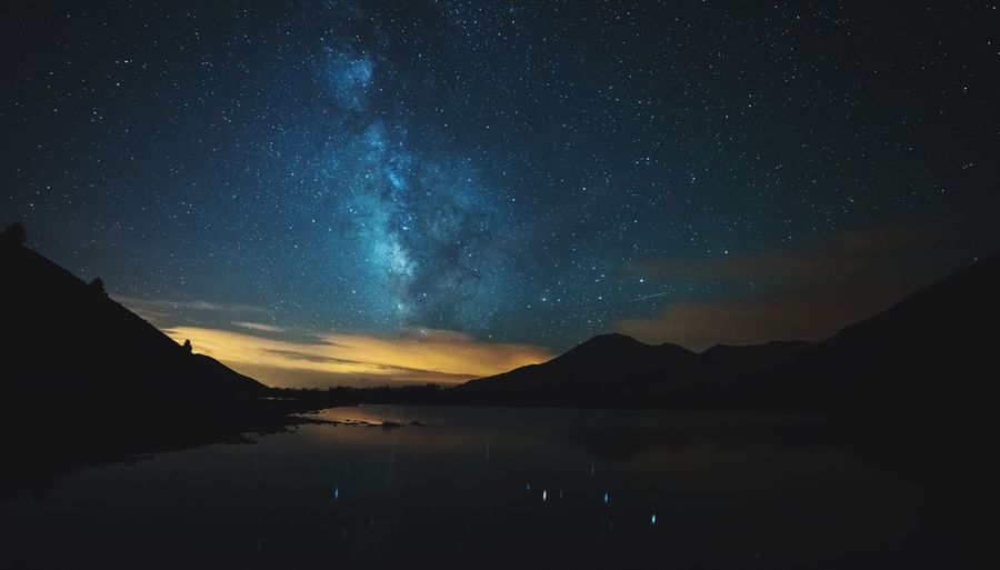 Scenic view of lake by silhouette mountains against sky at night