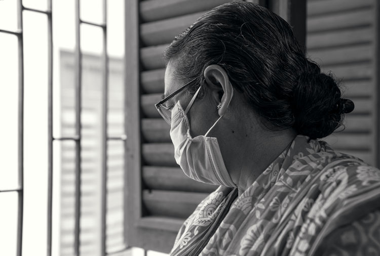 An aged bengali woman wearing surgical face mask, casually looking out of window