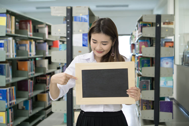 Smiling young woman pointing at writing slate in library
