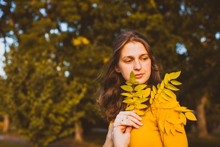 Portrait of young woman standing against yellow flowering plants