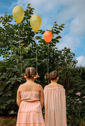REAR VIEW OF WOMAN WITH BALLOONS AGAINST PLANTS
