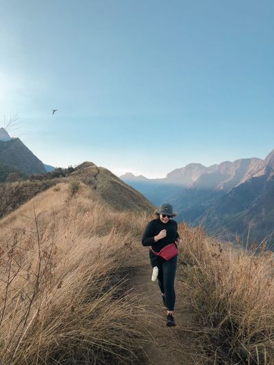 Full length of woman running on mountain ridge against sky