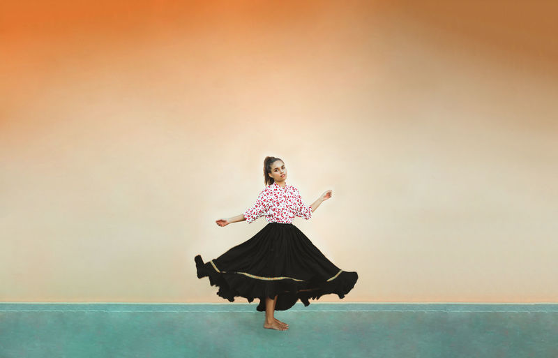 Woman wearing a skirt, dancingagainst orange wall