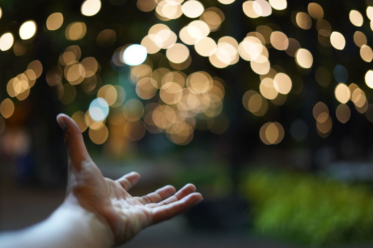 Cropped image of hand against illuminated lights at night