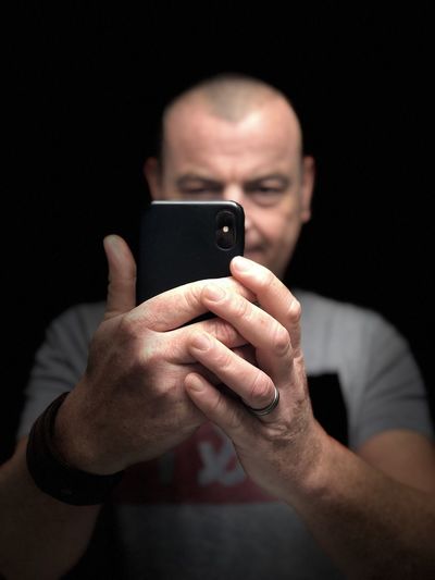 Portrait of man using mobile phone against black background