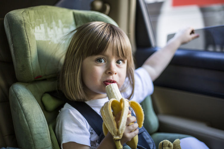Portrait of cute girl eating banana while sitting in car