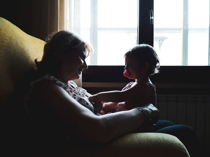 Grandmother playing with granddaughter while sitting on sofa at home