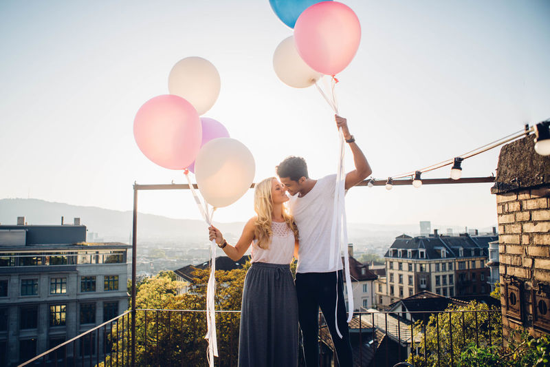 Couple standing with balloons against sky