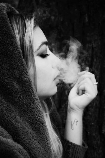Side view of young woman exhaling smoke against black background
