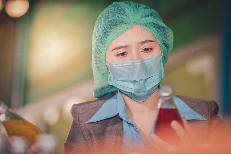 Close-up of woman wearing mask inspecting drinks in factory