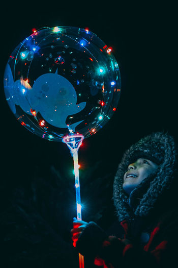Cute boy holding illuminated balloon against black background