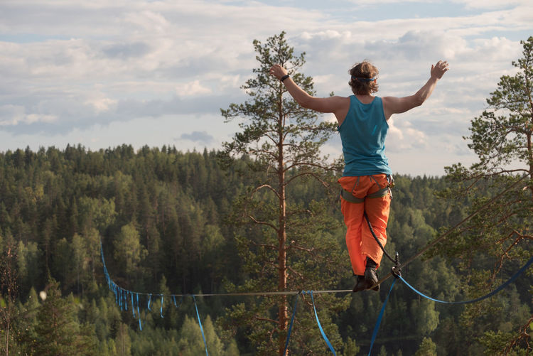 A tightrope walker walks along a long highline above the forest. back view