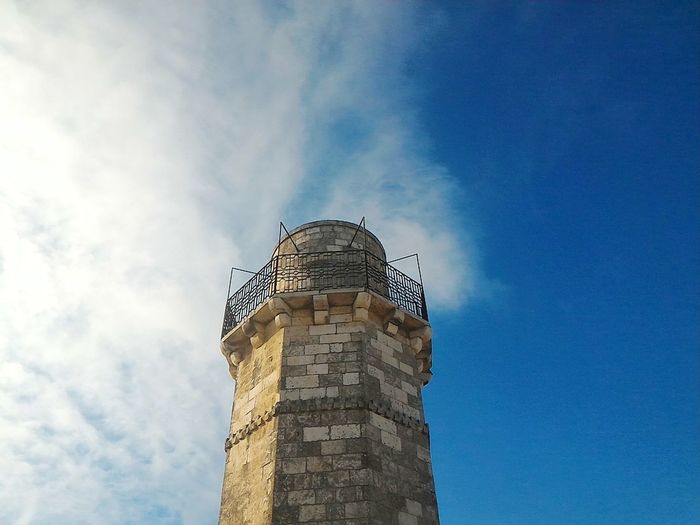 Low angle view of tower against cloudy blue sky on sunny day