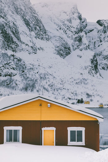 Snow covered house by building against sky