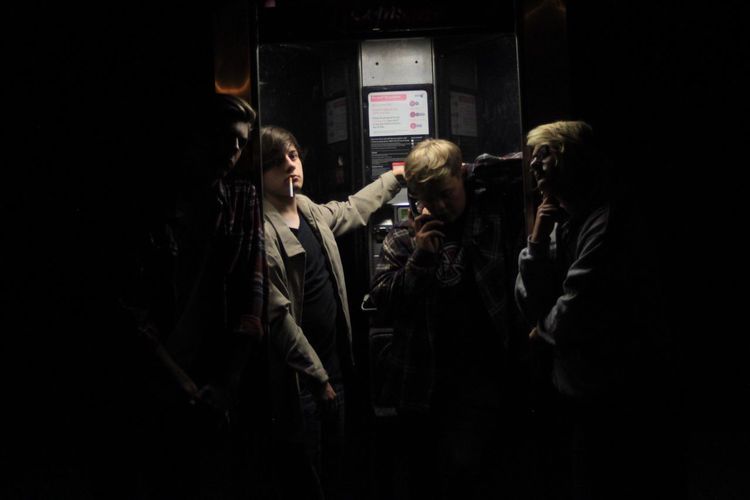 Young friends standing by telephone booth at night