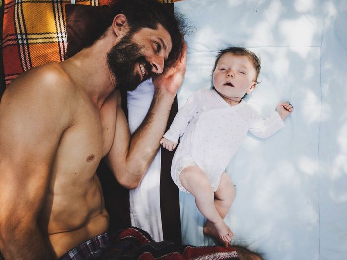 Directly above shot of shirtless father lying with toddler daughter on bed