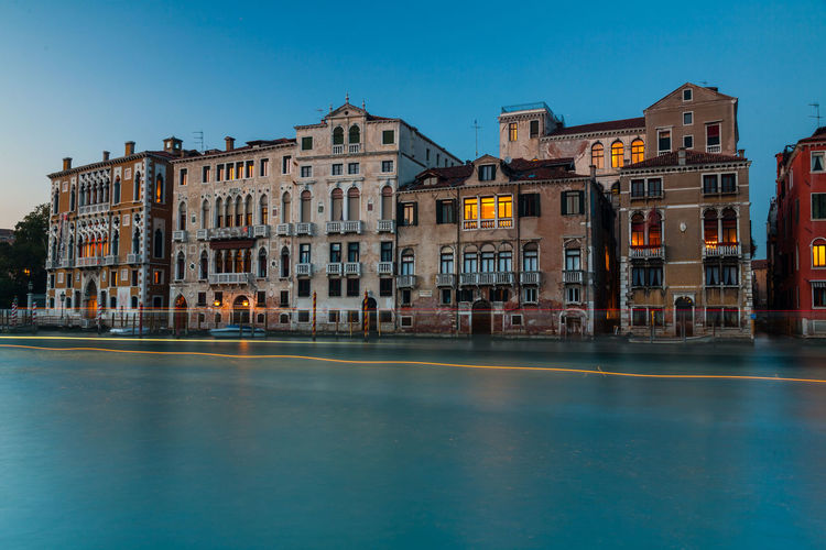 Buildings by canal against clear blue sky during sunset