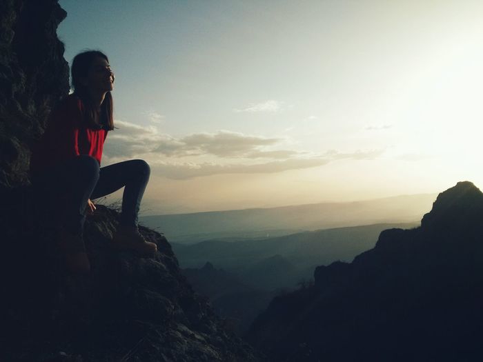 Young woman sitting on mountain against sky during sunset