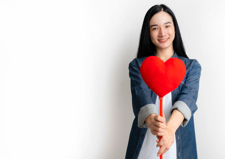 Portrait of a smiling young woman holding heart shape over white background