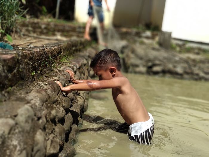 Side view of shirtless boy playing in water