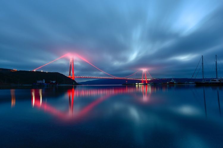 Illuminated suspension bridge over sea against sky
