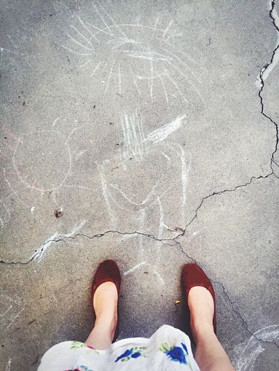 Low section of woman standing by chalk drawings on road