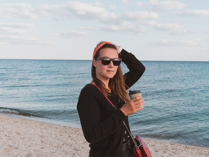 Pretty hipster woman walking on beach coffee cup lifestyle millennial girl drinking tea generationz 
