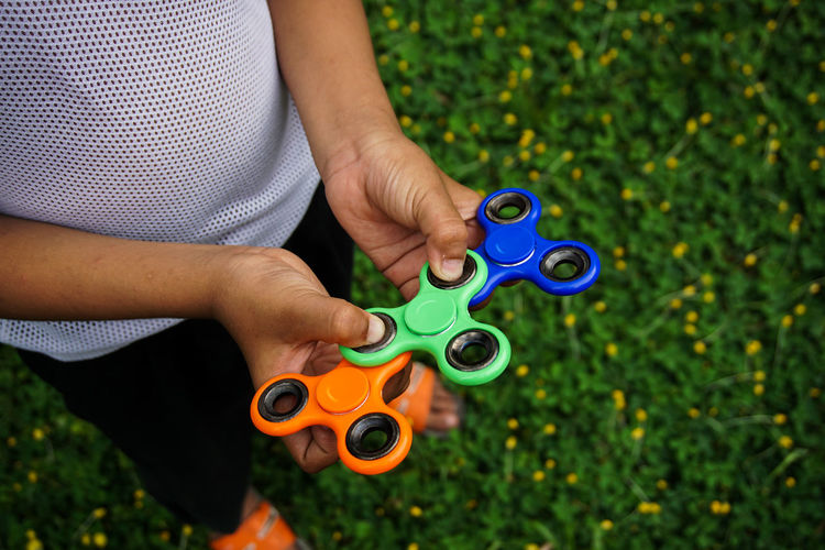 Low section of man holding colorful fidget spinners on grassy field