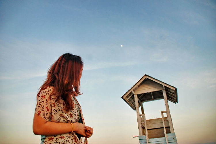 Low angle view of woman looking at lifeguard house against sky