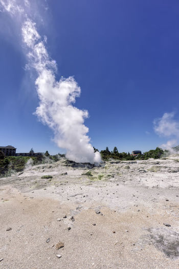 Smoke emitting from volcanic landscape against blue sky