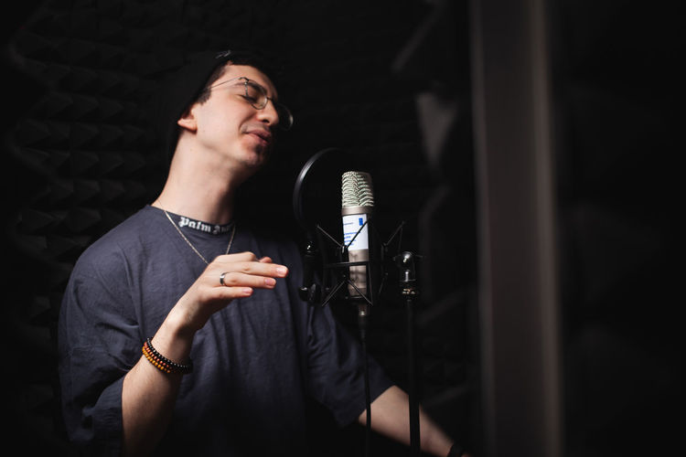 Man sings into microphone, professional recording studio, headphones. black soft walls, 
