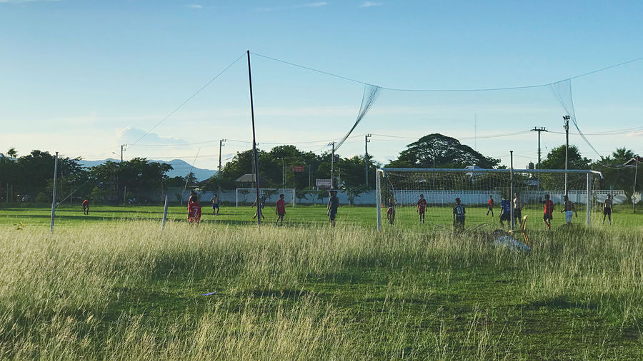 People playing soccer field against sky