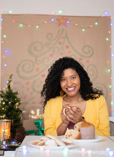 Portrait of smiling woman holding coffee cup sitting against christmas decoration