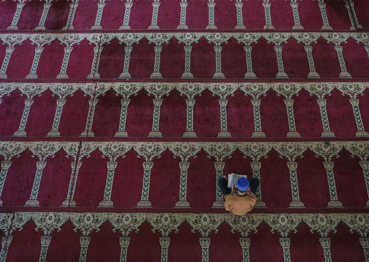 High angle view of man reading quran while sitting on carpet in mosque