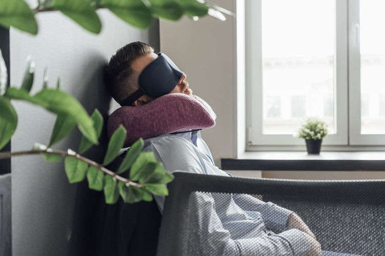 Exhausted businessman with eye mask and neck pillow sleeping in office