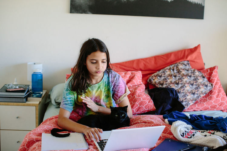 Tween girl works on her laptop for school with her cat on her lap