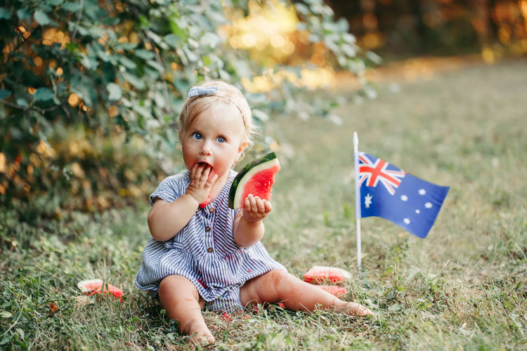 Cute adorable caucasian baby girl eating ripe watermelon with australian flag on ground. 