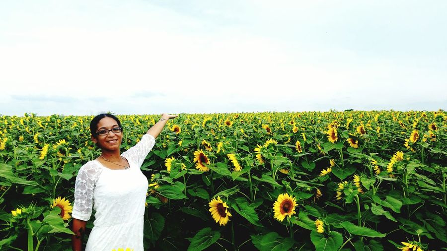 Portrait of smiling woman standing on sunflower field against sky