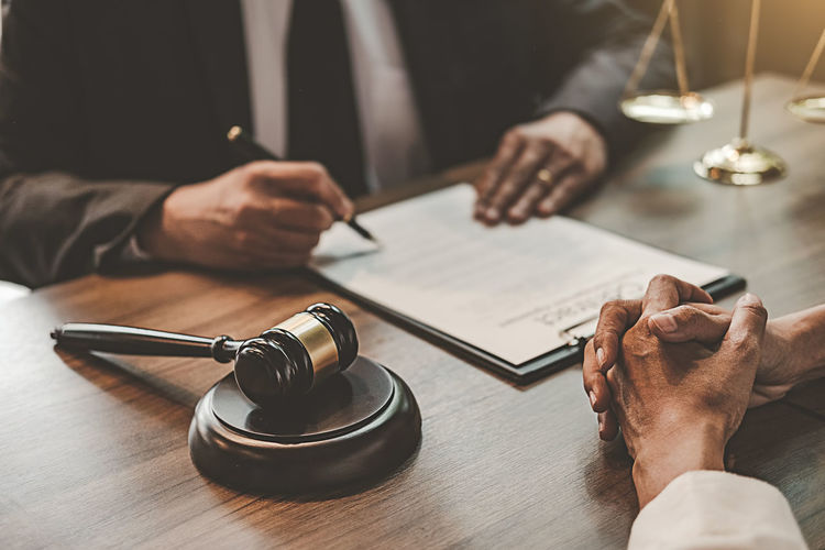 Judge signing contract while client sitting with hands clasped at table in office