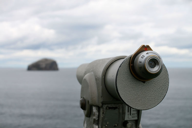 Close-up of coin-operated telescope by sea looking at rock and sea