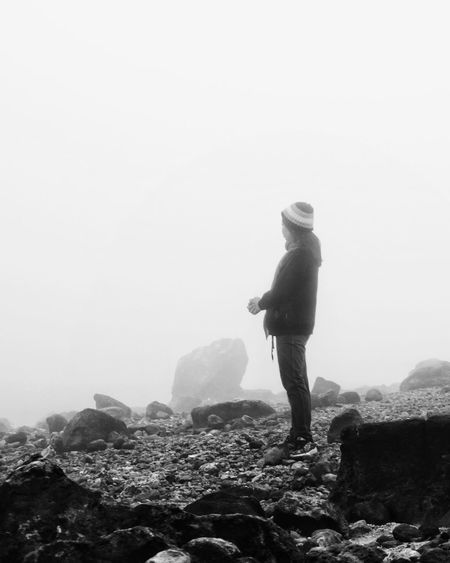 Side view full length of woman standing on rock against sky during foggy weather