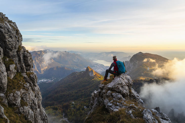 Pensive hiker looking at view while sitting on mountain peak during sunrise at bergamasque alps, italy