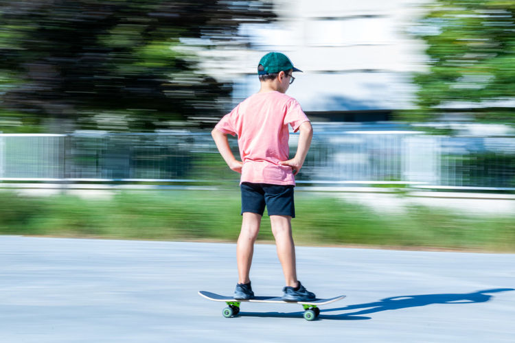Full length rear view of boy skateboarding on road