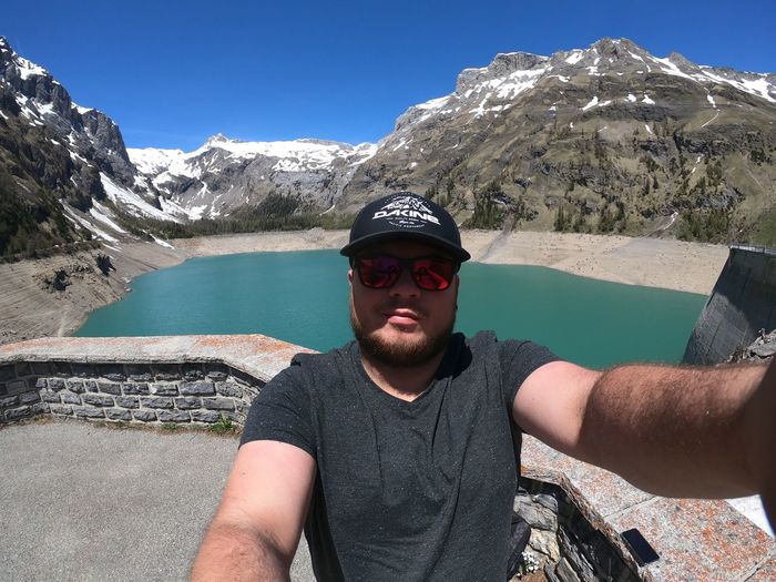 Portrait of young man in sunglasses against lake and mountains