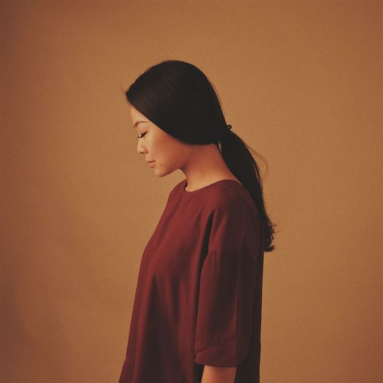 Side view of young woman standing over brown background