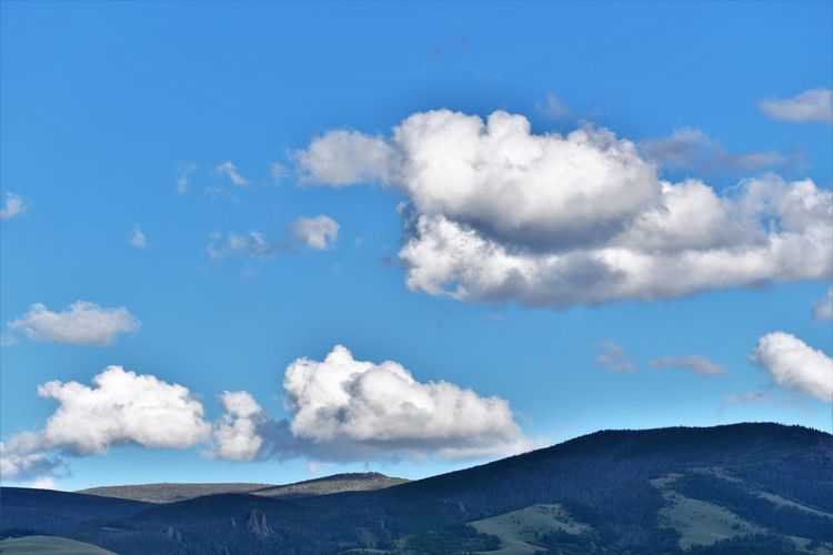 Low angle view of clouds over mountains against blue sky