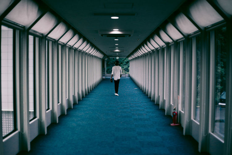 Rear view of man walking in empty corridor of building